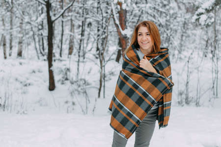 A happy young girl, wrapped in a plaid plaid and basking on a walk in the winter forest. A walk in the Christmas holidays, selective focus.の写真素材