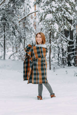 A happy young girl, wrapped in a plaid plaid and basking on a walk in the winter forest. A walk in the Christmas holidays, selective focus.の写真素材