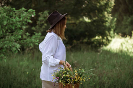 portrait of a happy girl with short hair in a black hat with a basket of flowers walking in a field.の写真素材