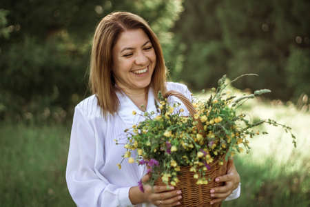 portrait of a happy girl with a short haircut with a basket of flowers walking in a field.の写真素材