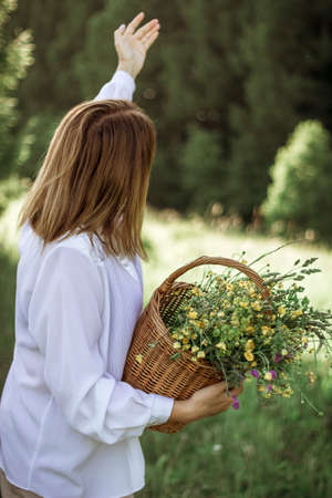 portrait of a happy girl with a short haircut with a basket of flowers walking in a field.の写真素材