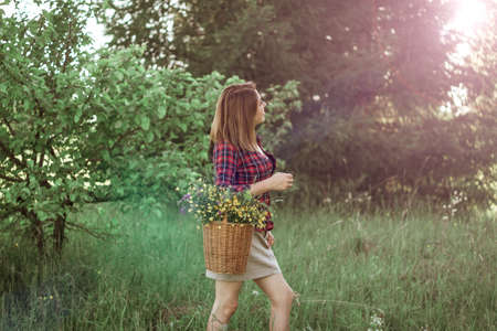 Summer lifestyle portrait of a beautiful young woman smiling and holding a basket with a bouquet of wild flowers. The concept of happiness and love.の写真素材