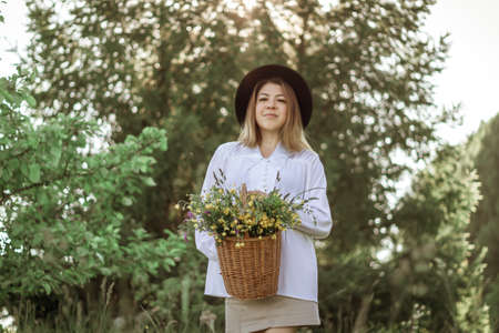 portrait of a happy girl with short hair in a black hat with a basket of flowers walking in a field.の写真素材