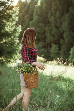 Summer lifestyle portrait of a beautiful young woman smiling and holding a basket with a bouquet of wild flowers. The concept of happiness and love.の写真素材