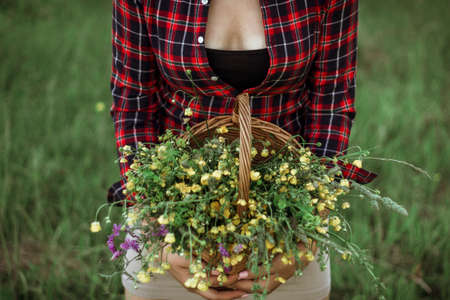 Summer lifestyle portrait of a beautiful young woman smiling and holding a basket with a bouquet of wild flowers. The concept of happiness and love. Photo without a head.の写真素材