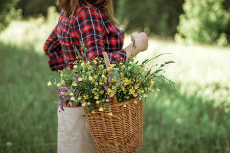 Summer lifestyle portrait of a beautiful young woman smiling and holding a basket with a bouquet of wild flowers. The concept of happiness and love. Photo without a head.の写真素材
