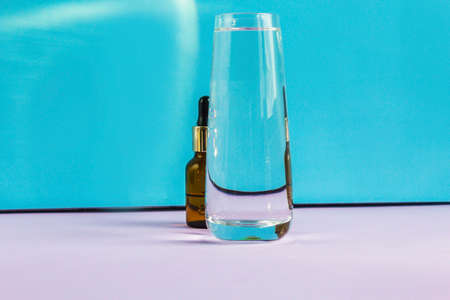 A glass of water and a cosmetic bottle with a pipette on a purple and blue background. Distort the picture through glass and water.の写真素材