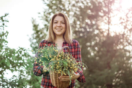 Summer lifestyle portrait of a beautiful young woman smiling and holding a basket with a bouquet of wild flowers. The concept of happiness and love.の写真素材