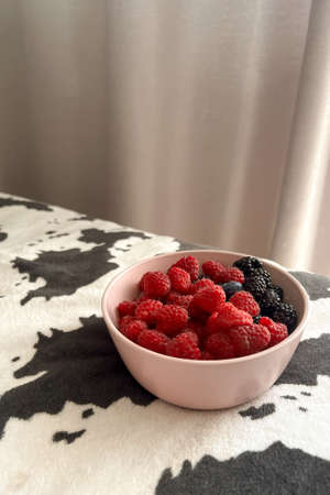 A pink cup with raspberries, blueberries and blackberries stands on a black and white background....