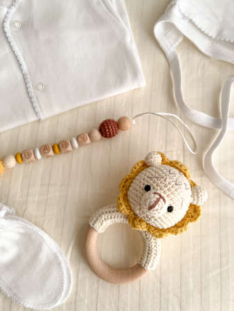 A baby's white suit, a hat for a newborn, scratches, socks, a rattle with a lion and a chain of wooden beads for teeth are lying on the bed. vertical photo.の写真素材
