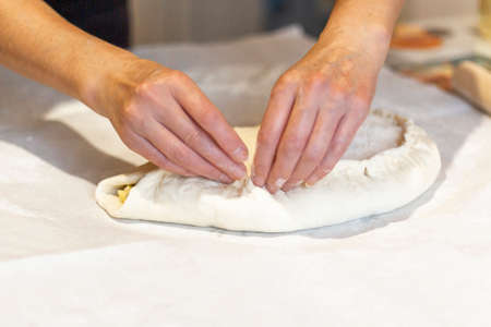 Women's hands sculpt from the dough a large pirok with potatoes and msyaom. home national cuisine.の写真素材
