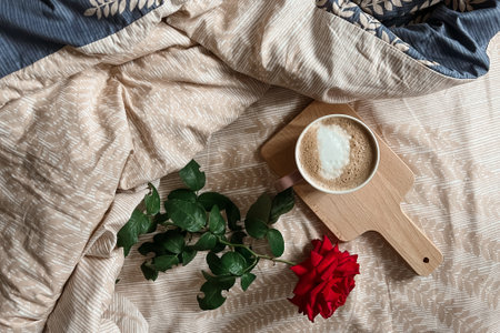 Top view of the morning breakfast in bed with cappuccino coffee on a tray and a red rose flower. Holiday greeting card.の写真素材