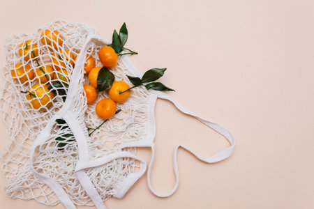 Top view of a white grocery eco-mesh cotton bag with fresh orange tangerines on a beige pastel background. Healthy food, zero waste, healthy lifestyle.の写真素材