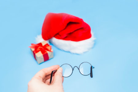 Santa Claus hat, a Christmas gift tied with a red ribbon through round Santa Claus glasses. selective focus. blur in glasses.の写真素材