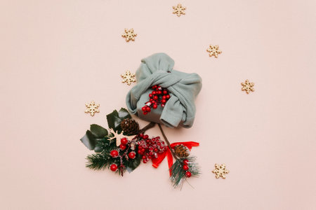 A Christmas gift, packed in olive-colored fabric and decorated with a twig with red berries, lies among spruce decorated twigs on a beige uniform background. christmas card. copyspace.の写真素材