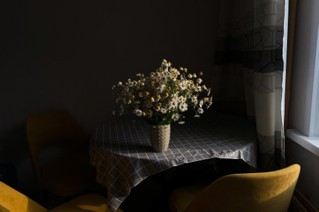 A bouquet of delicate chamomile in a ceramic vase. Morning light in the room. A vase with white...