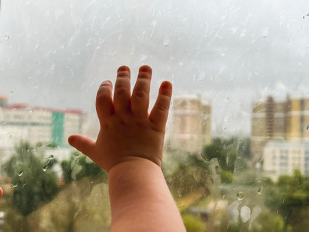 Baby's little hand on the cold glass of the window during the rain.の写真素材