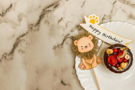 A small brownie chocolate cake on a plate with a golden candle and an ax with the inscription happy birthday, a cardboard lion.の写真素材