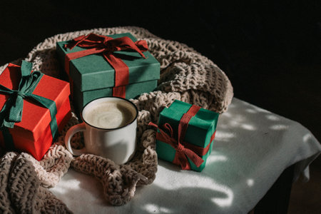 A white mug with coffee and milk stands in front of gift boxes in a dark room. Preparing a gift for...
