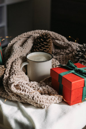 A white ceramic mug with cappuccino, a red gift box, cones are on the table. Winter composition....