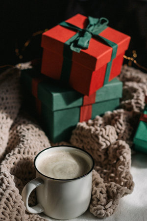A white ceramic cappuccino mug stands against the background of gift boxes. Preparation for gifts,...