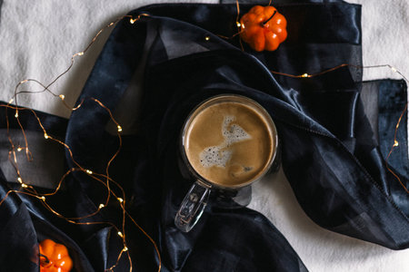 Black coffee in a glass mug on a table with a black tablecloth and orange pumpkins. Autumn table decoration. Top view.の写真素材
