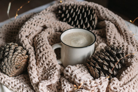New Year, Christmas card. Coffee with milk in a white mug among the cones wrapped in a warm knitted...