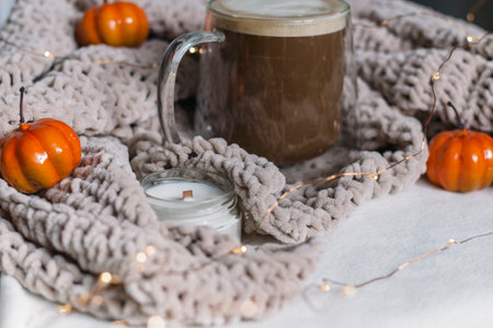Autumn cozy still life. Black coffee with milk in a glass mug on the table in a warm beige knitted plaid and orange pumpkins. A place for the text. Thanksgiving and Halloween.の写真素材