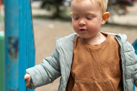 A little red-haired boy climbs the stairs on the playground and holds on to the handrail. Outdoor...