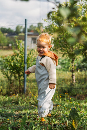 A little red-haired boy in a gray-blue jumpsuit walks around the garden area.の写真素材
