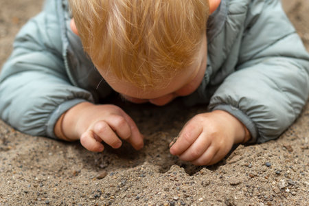 A happy little boy is lying on the sand and playing. A walk in the fresh air in spring.の写真素材