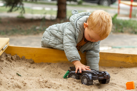 A red-haired boy sits on a sandbox and plays with a toy. Outdoor exercise, development of fine motor skills, creativity and thinking.の写真素材
