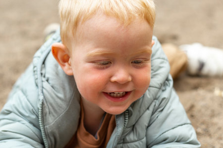 A happy little boy is lying on the sand and playing. A walk in the fresh air in spring.