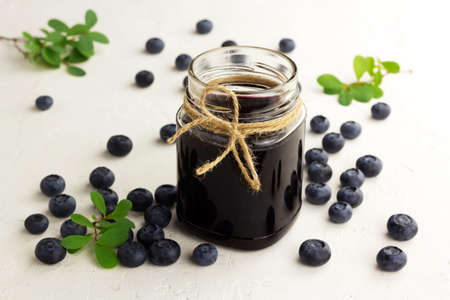 Bluberry jam in a glass jar and fresh blueberries on a light backgroundの写真素材