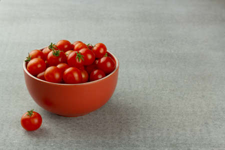 Cherry tomatoes in a red bowl on gray background with copy spaceの写真素材