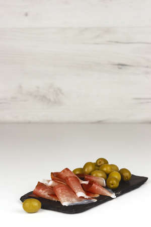 Spanish hamon or italian proscuitto and green olives on a slate. Vertical orientation with copy spaceの写真素材