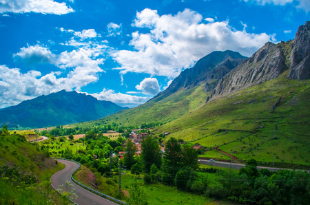 Amazing summer view on little town, blue cloudy sky and huge green rocky mountains on background with serpentine road taken from the highway near Santiago de Compostela. Galicia, Spainの写真素材