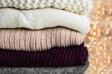 Warm knitted sweaters. Pile of knitted clothes on warm background, sweaters, knitwear, space for text, Autumn winter concept.の写真素材