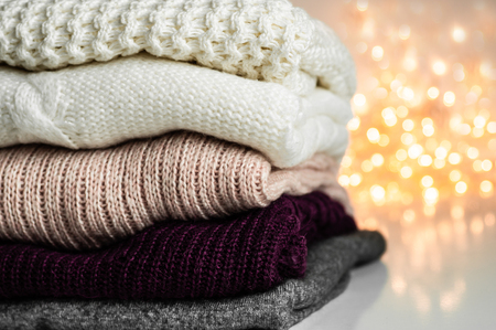 Warm knitted sweaters. Pile of knitted clothes on warm background, sweaters, knitwear, space for text, Autumn winter concept.の写真素材