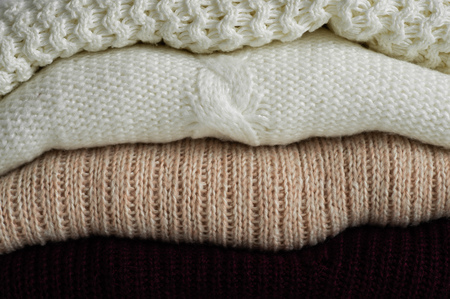 Warm knitted sweaters. Pile of knitted clothes on warm background, sweaters, knitwear, space for text, Autumn winter concept.の写真素材