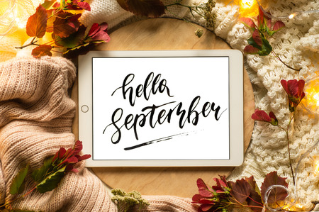 The tablet says the word hello September with red leaves and a dais on the wooden background. Concept of the autumn View from above. Copy Space.の写真素材