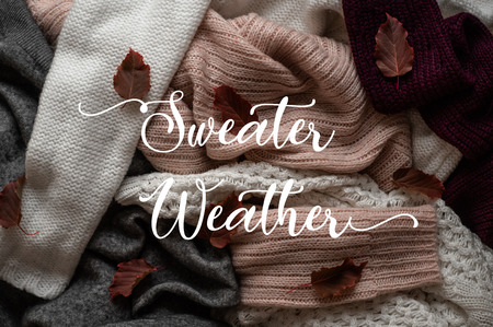 Background with warm sweaters and the inscription SWEATER WEATHER. Pile of knitted clothes with autumn leaves, warm background, knitwear, Autumn concept.の写真素材