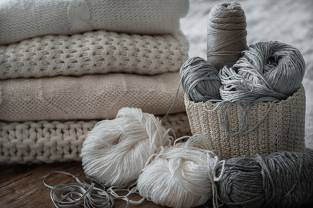 A woven basket with white and gray thread for knitting and knitting needles. White sweaters and yarn for knitting closeup.の写真素材