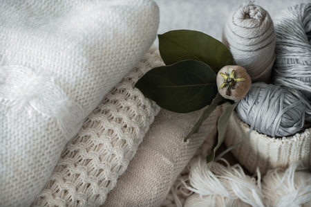 A woven basket with white and gray thread for knitting and knitting needles. White sweaters and yarn for knitting closeup.の写真素材