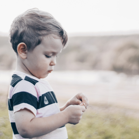 Happy child, little boy looks down, pensive look and holding in hands the growths outdoors. Space for Your Text. Retro toned. Summertimeの写真素材