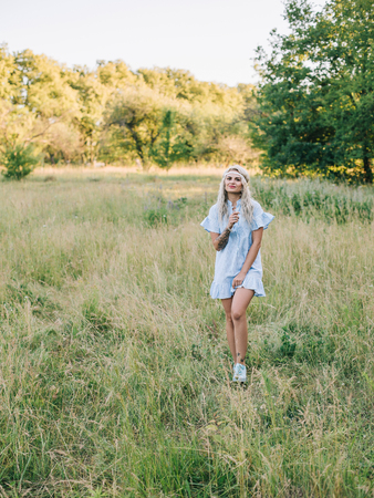 Portrait of a beautiful girl in a blue dress with a headache in a field at sunset in summer. Casual summer clothes. Close-up.の写真素材