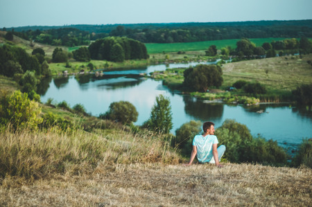 Young Man Sitting on a hill in a grass and enjoying the majestic landscape of nature and Enjoying the View. Winner  Success concept.の写真素材
