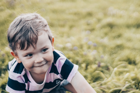 Happy child, little boy looks down, pensive look and holding in hands the growths outdoors. Space...