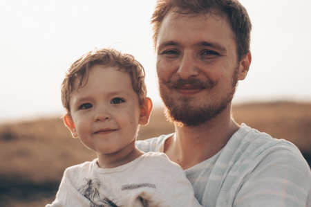 Happy kid playing with father. Dad and son outdoors. Father carrying child on his back. Happy family in summer field.の写真素材