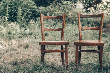 Pair old wooden chair outdoors. Two wooden folding chairs for rest. Around the lush grass and white flowers. Solar glare is played on a wooden surface. The environment offers privacy.の写真素材